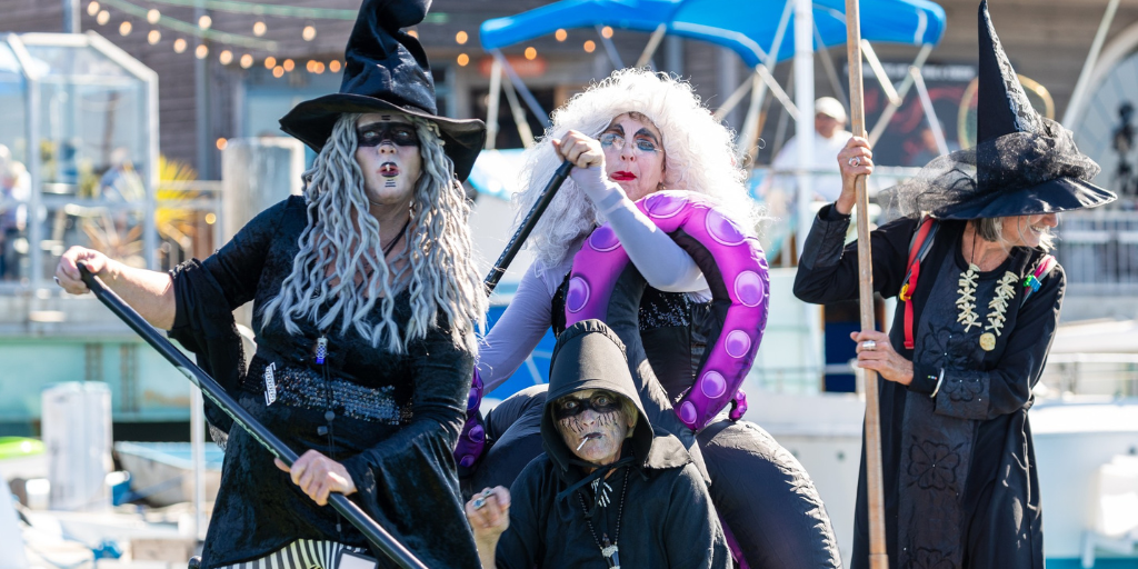 Four women dressed in witches costumes paddle out on Morro Bay (2023)